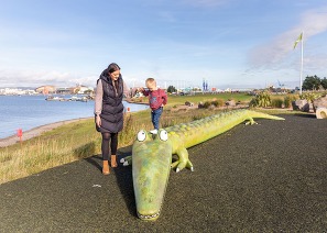 Parent and toddler by a bench shaped like a crocodile Cardiff Bay
