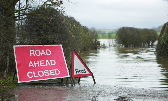 Picture of a flooded road with a sign saying 'flood' in front of it
