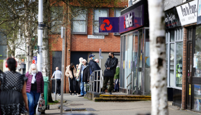 Street scene in Headington, Oxford. People queue outside shops. 