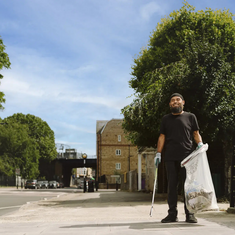 A smiling man holding a litter pick and plastic waste sack