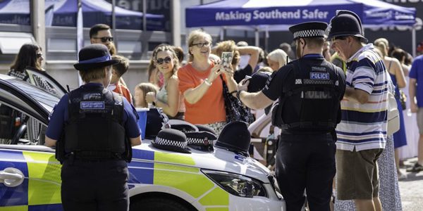 Two officers and a police car surrounded by open day visitors trying on helmets and hats