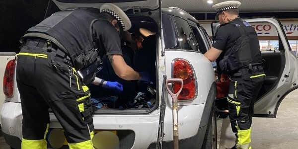 Two uniformed police officers searching a white mini car