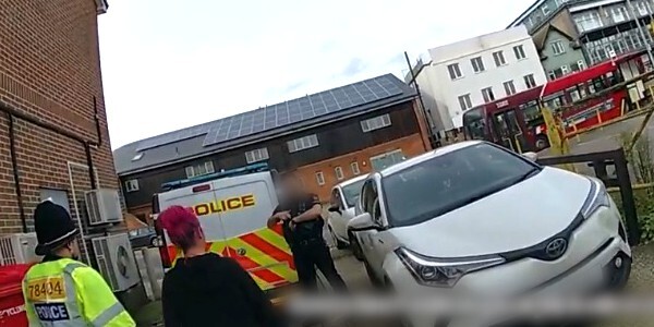 Body worn camera video still image of two officers arresting a woman with pink hair.