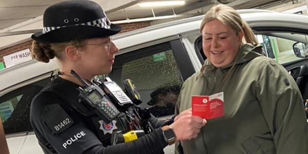 Police officer explaining leaflet about modern slavery and human trafficking to a member of the public at a car wash