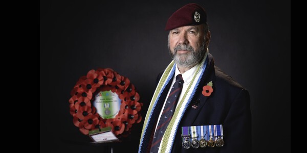 David Gillies, wearing a South Atlantic Medal Association scarf and war medals. A poppy wreath is in the background