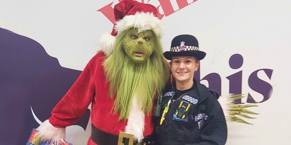 Person in Grinch costume posing with a female police officer in uniform