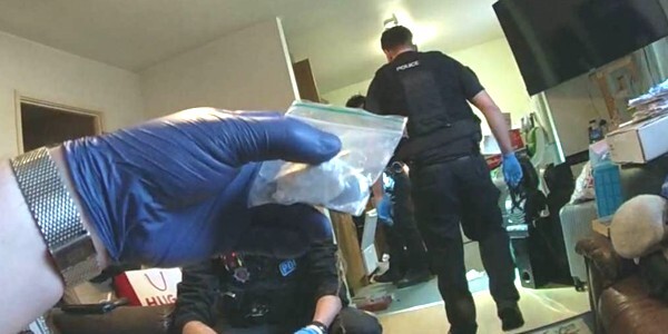 plastic bag containing white drugs held by a hand wearing a blue plastic glove