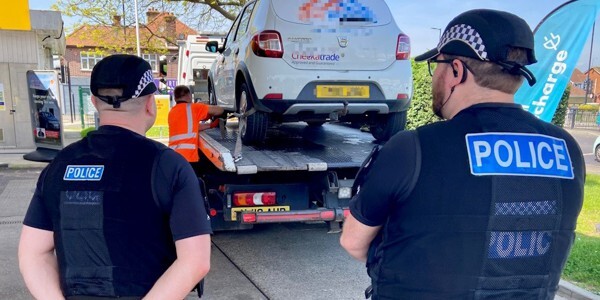 Two officers supervising while a white van is loaded onto a trailer
