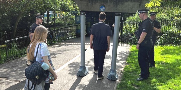 A knife arch deployed in Chelmsford on a footpath. Three police officers watch man walk through with woman watching