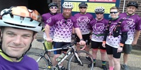 Seven riders in cycling gear pose in their purple sponsored cycling tops;