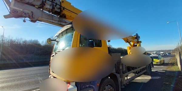 Yellow truck with crane stopped on M25 with police car behind