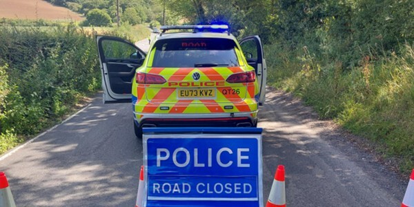 Police car with 'Road Closed' sign and cones closing off a narrow country lane