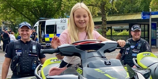 Smiling girl sitting on a police jetski with two police officers either side