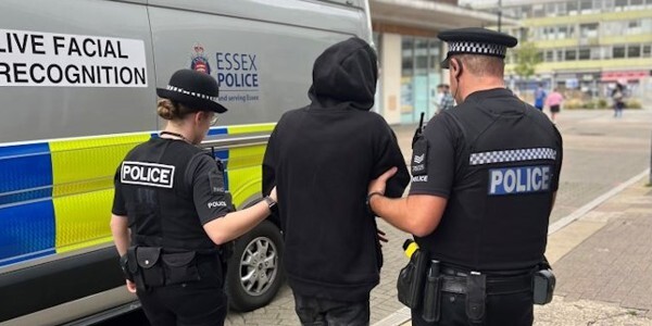 Man in black hoodie being led away by two police officers in Harlow next to a live facial recognition van