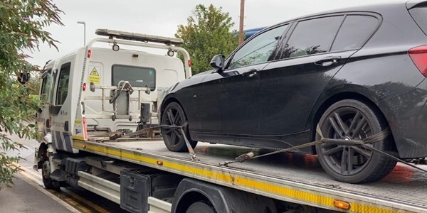 Black car being recovered on the back of a flatbed lorry