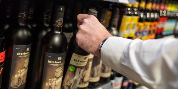 Hand taking a bottle of red wine from a shop display