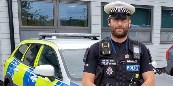 Wayne David in uniform standing next to a police patrol car