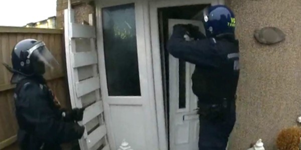 Officers breaking a front door to gain access to a house during a drugs raid