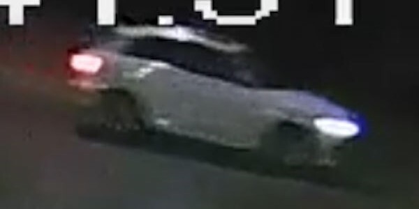 Image of a light-coloured car at night with lights on from a CCTV camera