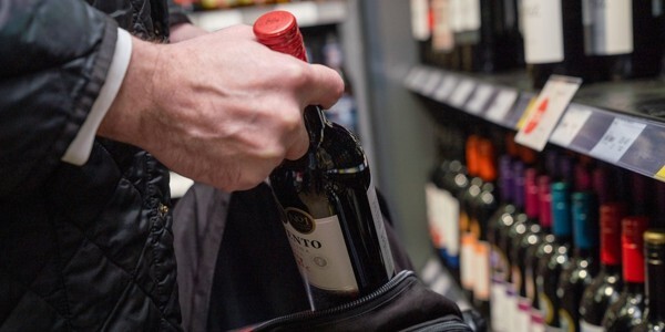 Shoplifter's hand taking a bottle of red wine from the shelf