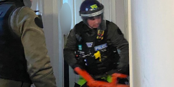 Officers in protective uniform using red hammer to enter a premises
