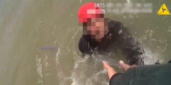 Person in red helmet being helped out of the water by Marine Unit officers