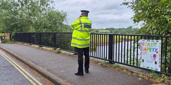 Police officer conducting a speed check on a bridge with a road safety poster designed by children on the railings
