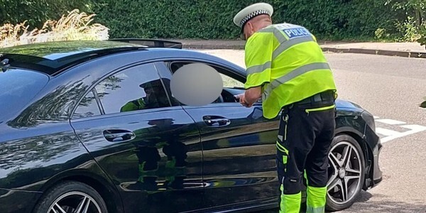 Roads policing officer speaking to a driver of a black car through the open window. The driver's face is blurred