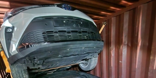 A white car piled on top of another car in a shipping container