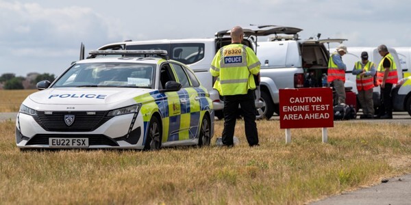 Police officer standing next to a police car with various other investigators and their vehicles nearby on the airfields at Southend Airport
