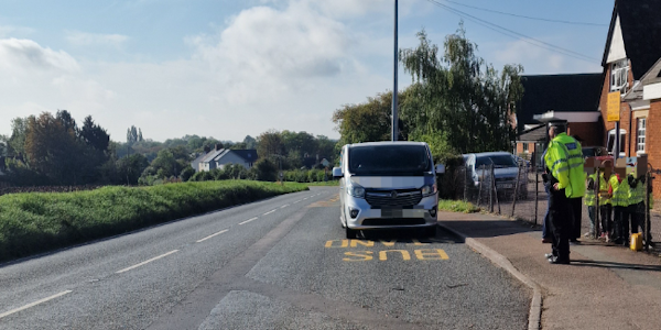 Students and Police officers speaking to a silver van parked outside the school
