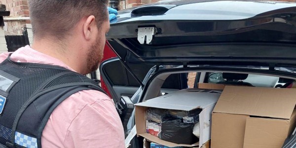 Officer in front of car boot loaded with Illegal vapes and tobacco worth over £60,000