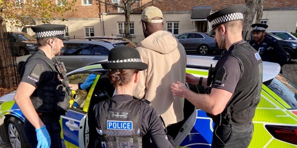 Four officers detain a man and place him into the back seat of a police car