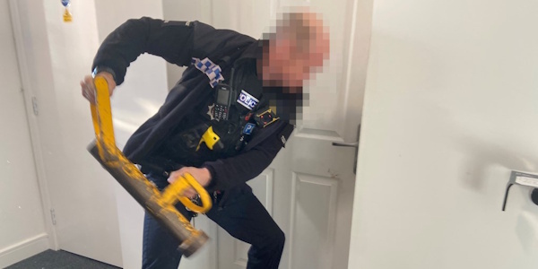 Police officers opening a door with a yellow ram hammer