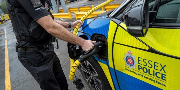 Police officer holding a charging cable next to an electric police car