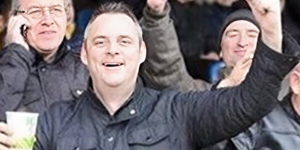 Simon Dobbin holding a paper cup and smiling as part of a crowd