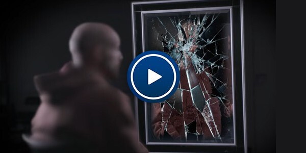 Man being interviewed in front of a smashed mirror