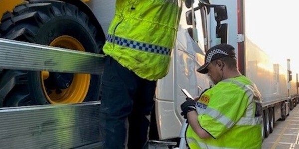 Two officers inspecting a lorry loaded with construction vehicles