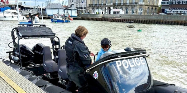 Police officer speaking with a person on a small police boat moored by a harbour,