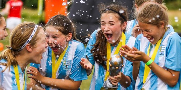 Girls wearing blue and white football kit with yellow braided medals and holding trophy celebrating their win