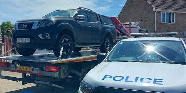 Large black 4x4 vehicle recovered and on the back of a transporter lorry with a police car in the foreground
