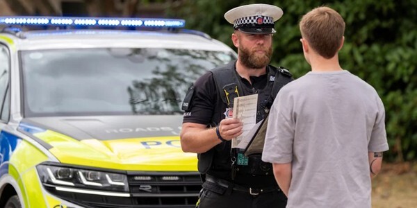 Roads policing officer speaking to a driver at the side of the road with a police car behind him.