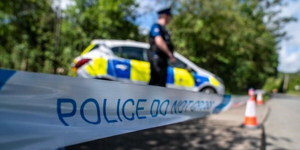 An officer guarding a scene behind police tape