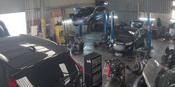 Interior of the chop shop garage with a car up on a ramp and various other tools and vehicles