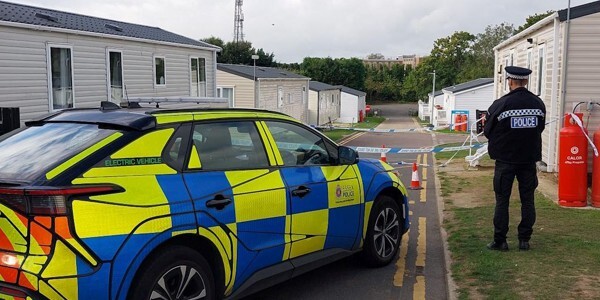 Officer next to police car guarding the scene at Vale Farm Holiday Park.