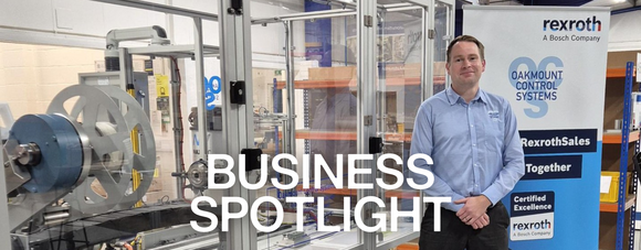 A man in a blue shirt stands in a modern industrial workspace next to large automated machinery.