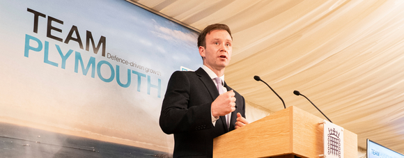 Fred Thomas at a podium during the Team Plymouth event, with the words "Defence-driven growth" on a banner behind.