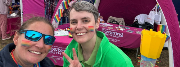 Two team members smiling in front of a Fostering South East gazebo at UK Pride