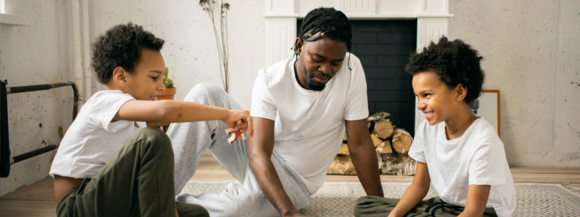 Man sitting on a rug playing a game with two young boys