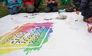 Child Friendly Borough logo on a banner with children writing 